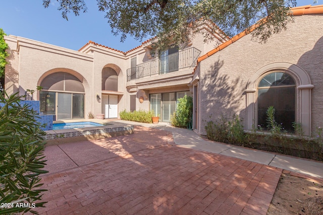 rear view of property with a balcony, a patio, and a hot tub