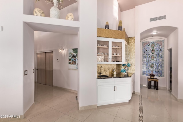 bar featuring sink, light tile patterned floors, backsplash, a towering ceiling, and white cabinets