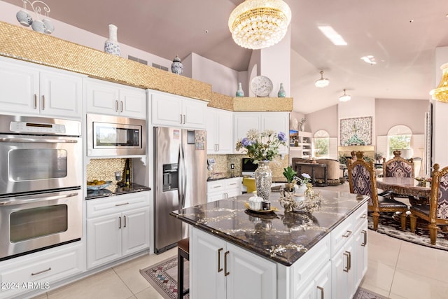 kitchen featuring stainless steel appliances, white cabinets, dark stone counters, lofted ceiling, and light tile patterned floors