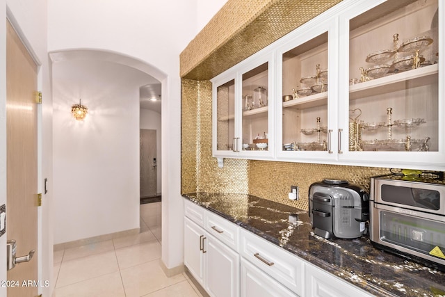 bar with decorative backsplash, light tile patterned floors, white cabinetry, and dark stone countertops