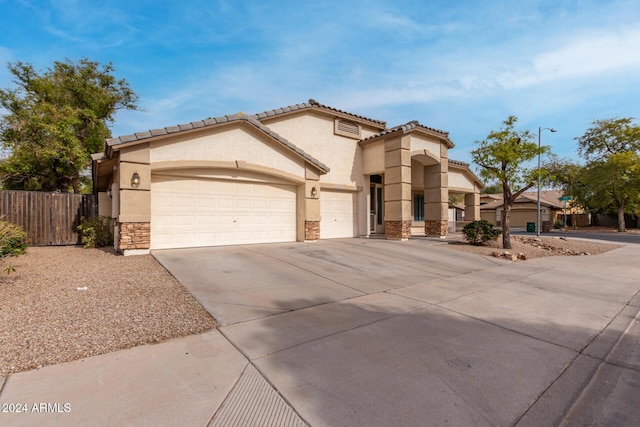 mediterranean / spanish-style home with fence, driveway, an attached garage, stucco siding, and stone siding