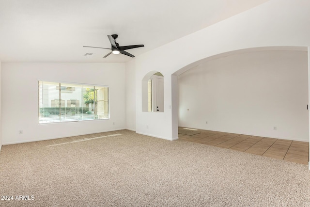 tiled empty room featuring arched walkways, a ceiling fan, carpet flooring, and vaulted ceiling