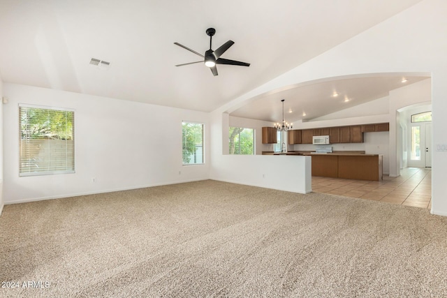 unfurnished living room featuring visible vents, light colored carpet, ceiling fan with notable chandelier, arched walkways, and light tile patterned flooring