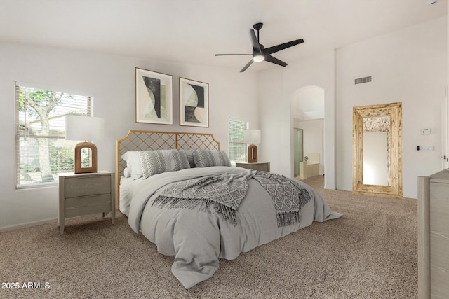 carpeted bedroom featuring ceiling fan, visible vents, arched walkways, and connected bathroom