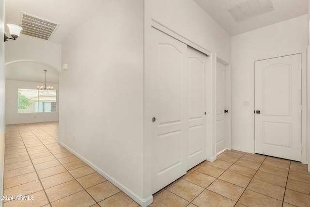 corridor with an inviting chandelier, light tile patterned floors, arched walkways, and visible vents