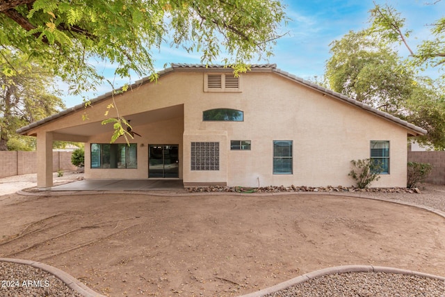 rear view of house with a patio area, stucco siding, a tile roof, and a fenced backyard