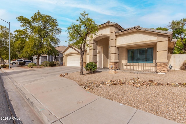 mediterranean / spanish home featuring a tiled roof, stucco siding, a garage, stone siding, and driveway