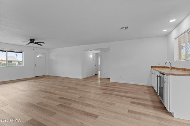 unfurnished living room featuring ceiling fan, light hardwood / wood-style floors, sink, and beverage cooler