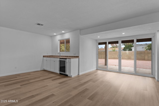 kitchen featuring white cabinets, a textured ceiling, light wood-type flooring, and beverage cooler