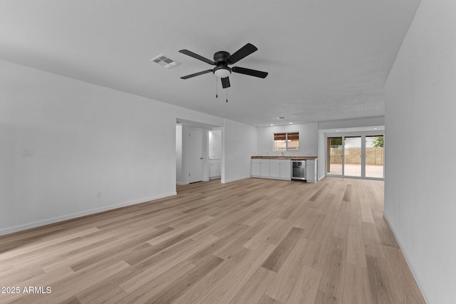 unfurnished living room with ceiling fan, light wood-type flooring, a textured ceiling, and wine cooler