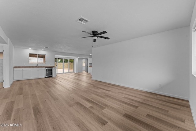 unfurnished living room featuring light hardwood / wood-style floors, wine cooler, and ceiling fan