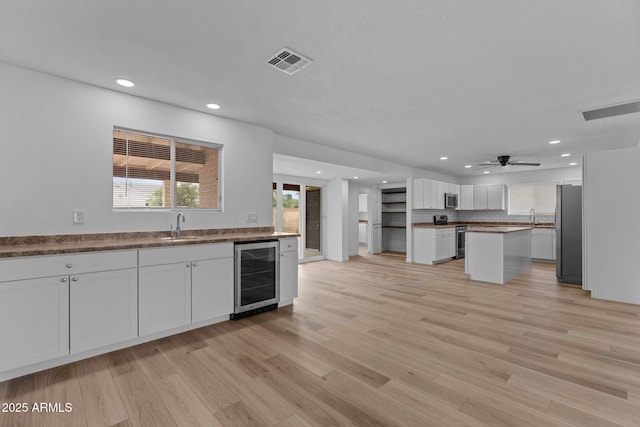 kitchen with white cabinetry, sink, stainless steel appliances, beverage cooler, and light hardwood / wood-style floors