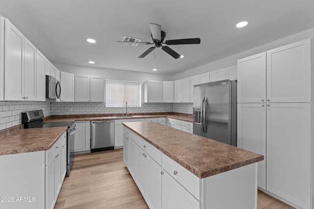 kitchen featuring appliances with stainless steel finishes, ceiling fan, sink, white cabinets, and a center island