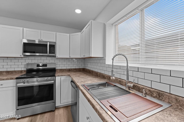 kitchen featuring sink, light hardwood / wood-style flooring, appliances with stainless steel finishes, tasteful backsplash, and white cabinetry