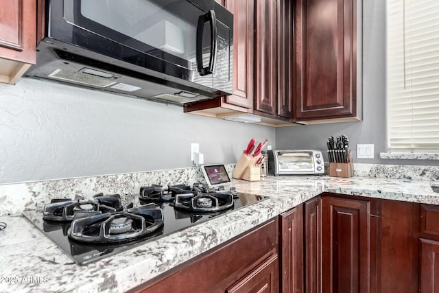 kitchen with light stone countertops, black appliances, a toaster, and dark brown cabinets