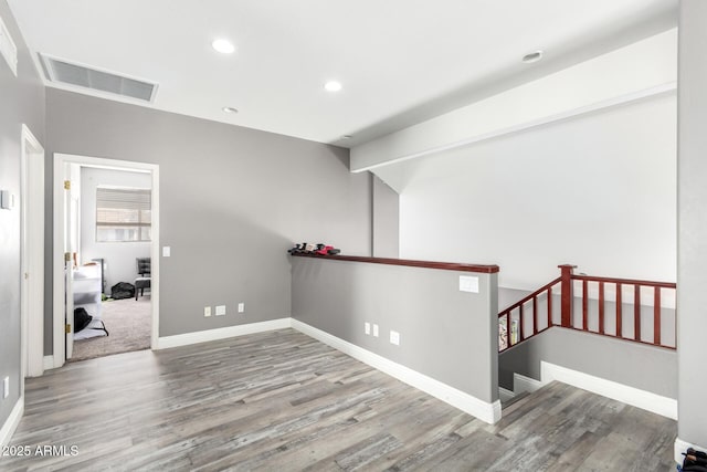 hall with baseboards, visible vents, wood finished floors, and an upstairs landing