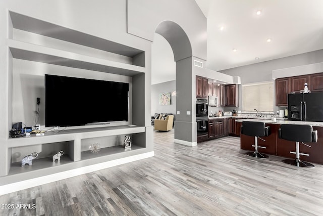 kitchen featuring a breakfast bar area, light countertops, black refrigerator with ice dispenser, light wood-style flooring, and dark brown cabinets