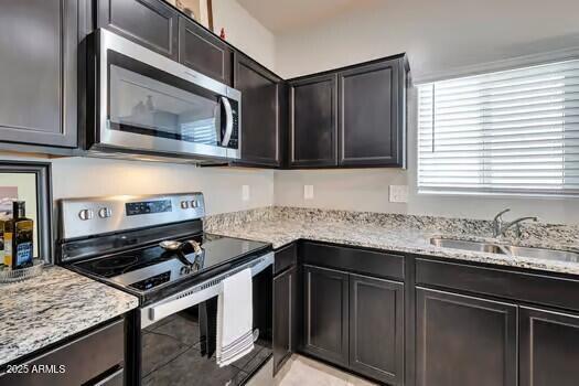 kitchen with dark brown cabinets, stainless steel appliances, light stone counters, and sink