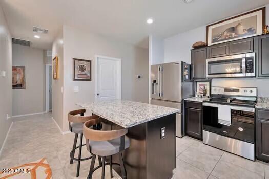 kitchen featuring light stone countertops, appliances with stainless steel finishes, light tile patterned floors, a kitchen island, and a breakfast bar area