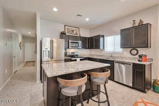 kitchen featuring light tile patterned flooring, appliances with stainless steel finishes, a kitchen island, a kitchen bar, and dark brown cabinetry