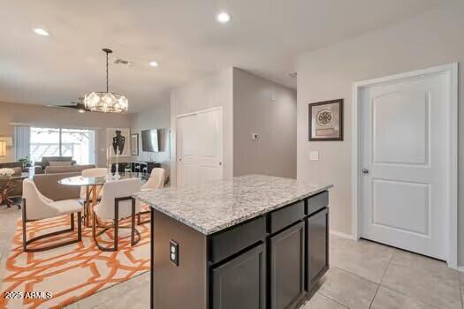 kitchen with ceiling fan, a kitchen island, light stone counters, pendant lighting, and light tile patterned flooring