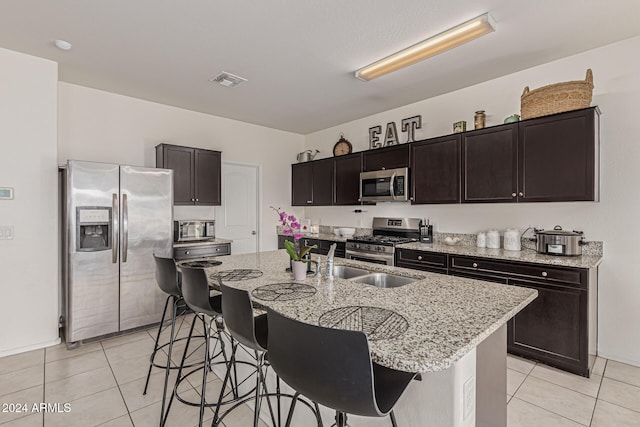 kitchen featuring appliances with stainless steel finishes, a breakfast bar, light stone countertops, and a center island with sink