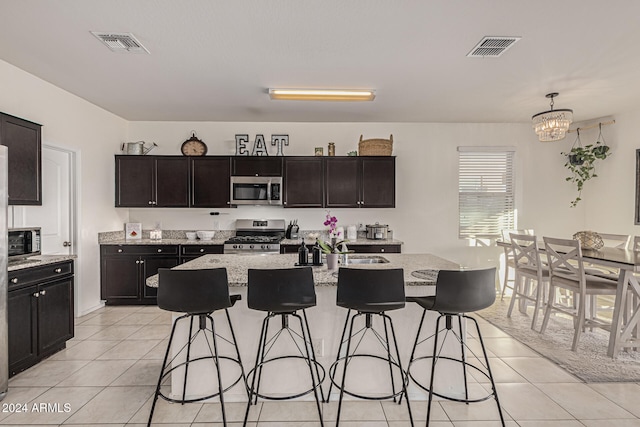 kitchen featuring appliances with stainless steel finishes, decorative light fixtures, and an island with sink