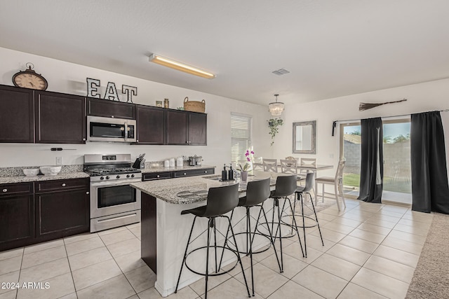 kitchen featuring light stone counters, appliances with stainless steel finishes, light tile patterned floors, and a kitchen island with sink