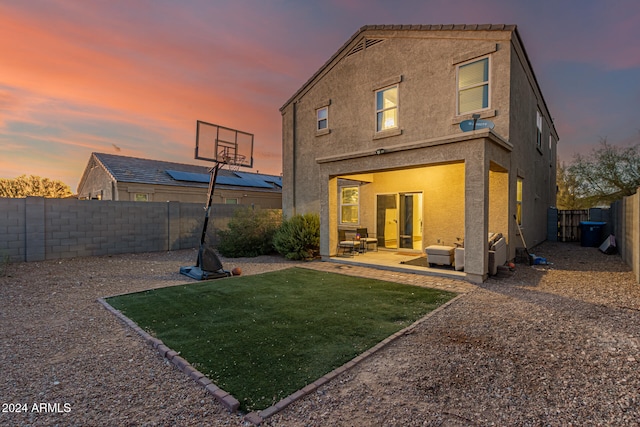 back house at dusk featuring a patio and a lawn