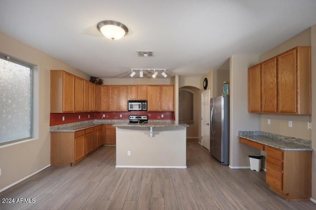 kitchen featuring a center island, light hardwood / wood-style flooring, light stone countertops, appliances with stainless steel finishes, and a breakfast bar area