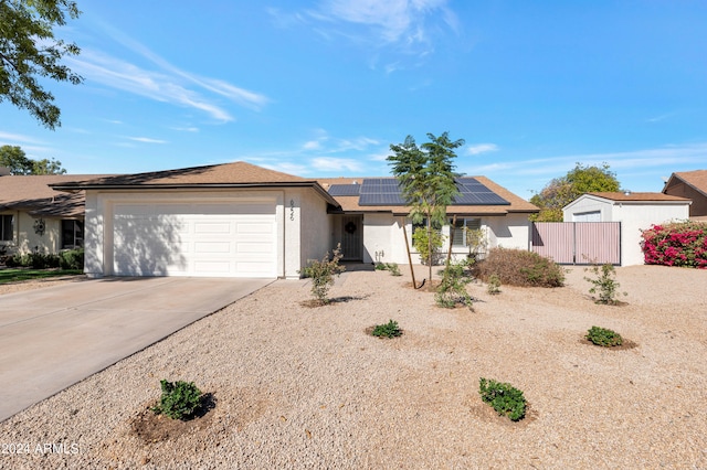 single story home featuring stucco siding, concrete driveway, an attached garage, roof mounted solar panels, and fence