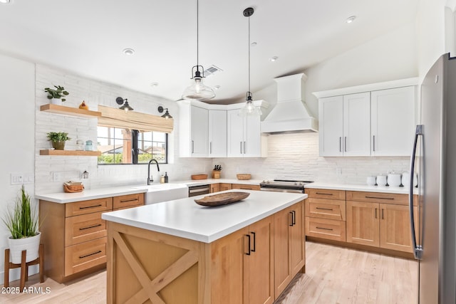 kitchen with appliances with stainless steel finishes, light countertops, custom range hood, and a sink
