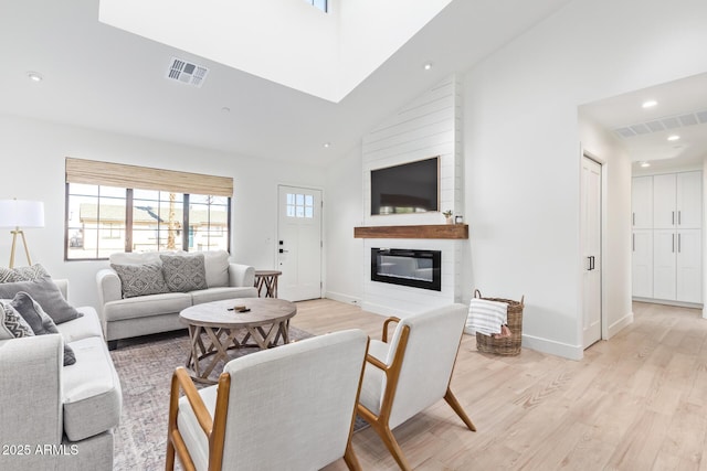 living room featuring light wood-type flooring, a fireplace, high vaulted ceiling, and visible vents
