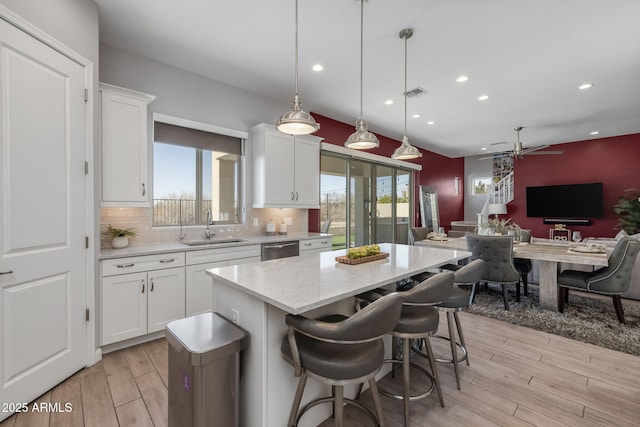 kitchen with pendant lighting, sink, white cabinetry, a kitchen island, and stainless steel dishwasher