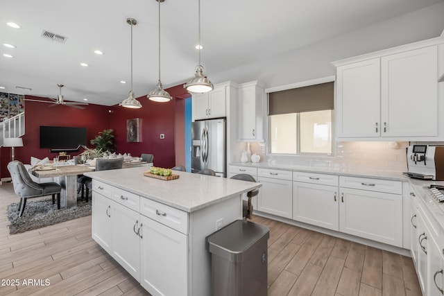 kitchen with pendant lighting, tasteful backsplash, white cabinets, light stone counters, and stainless steel fridge with ice dispenser