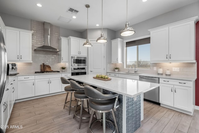 kitchen featuring wall chimney exhaust hood, sink, appliances with stainless steel finishes, a kitchen island, and white cabinets