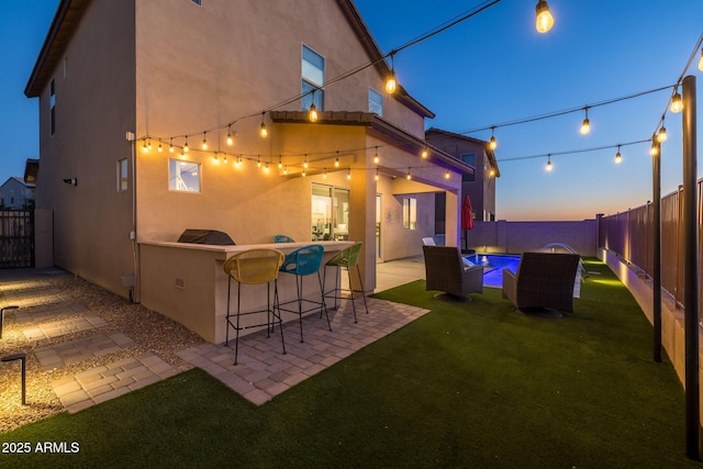 back house at dusk featuring a lawn and a patio