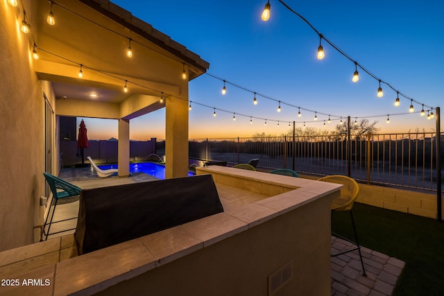 patio terrace at dusk with pool water feature, a fenced in pool, and an outdoor bar