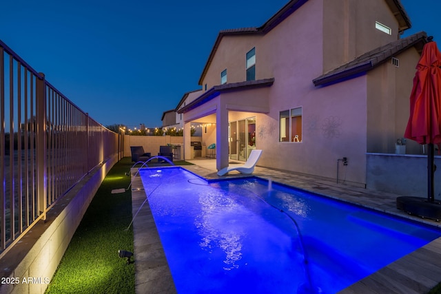 pool at night featuring pool water feature and a patio area