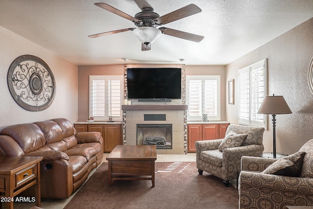 living room with ceiling fan, a large fireplace, light colored carpet, and a textured ceiling