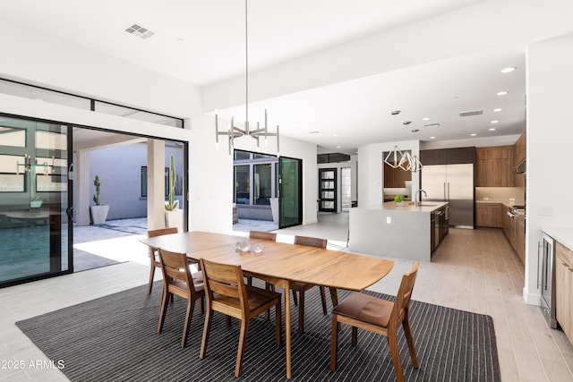 dining area with sink, light hardwood / wood-style flooring, a notable chandelier, and french doors