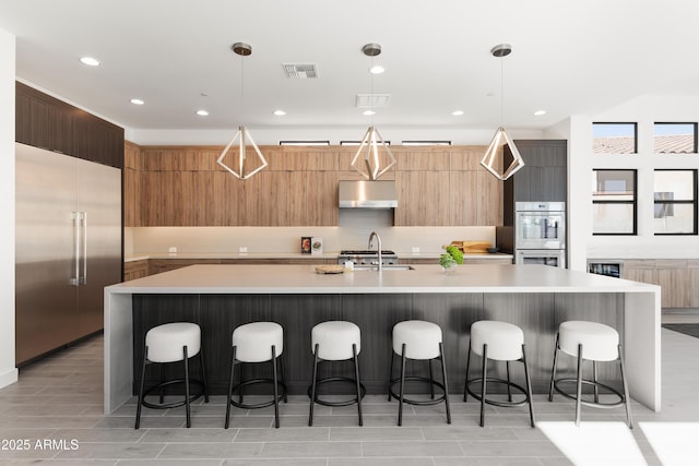 kitchen with built in refrigerator, a kitchen breakfast bar, a large island with sink, and decorative light fixtures