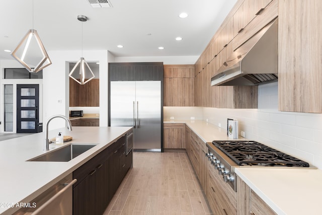 kitchen featuring appliances with stainless steel finishes, decorative light fixtures, sink, decorative backsplash, and light wood-type flooring