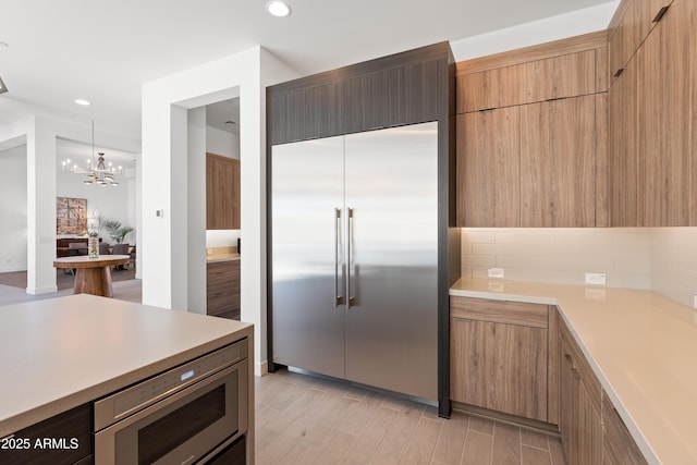 kitchen featuring tasteful backsplash, built in appliances, decorative light fixtures, and light wood-type flooring