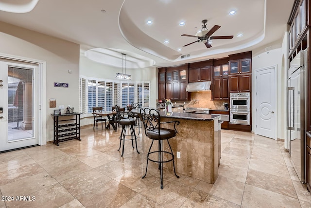 kitchen with pendant lighting, dark stone counters, a raised ceiling, ceiling fan, and double oven