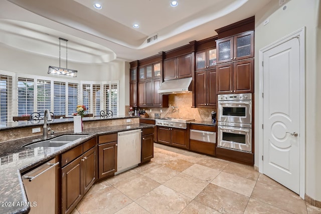 kitchen with sink, decorative backsplash, dark stone countertops, appliances with stainless steel finishes, and decorative light fixtures