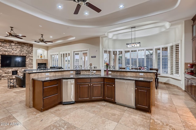 kitchen featuring stainless steel dishwasher, sink, dark stone countertops, hanging light fixtures, and an island with sink