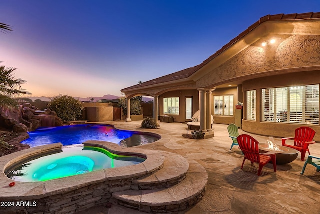 pool at dusk with an in ground hot tub, a patio, pool water feature, and an outdoor fire pit