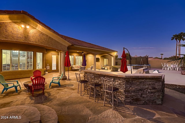 patio terrace at dusk featuring a bar, a trampoline, and ceiling fan