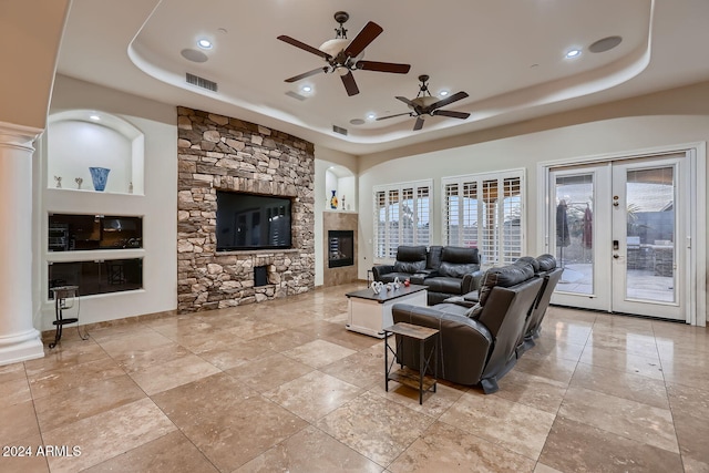 living room with ceiling fan, a stone fireplace, french doors, and a tray ceiling